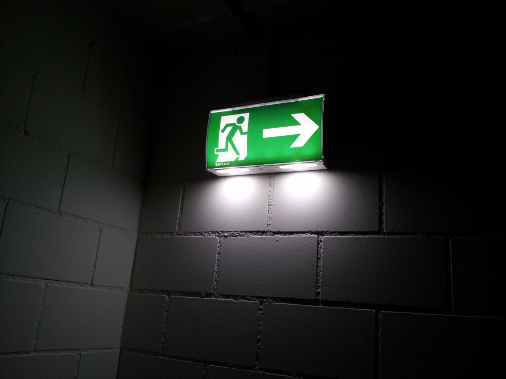 Zelené označení nouzového východu v tmavé chodbě.
