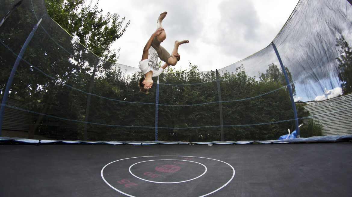 Člověk skáče na zahradní trampolíně s ochrannou sítí.