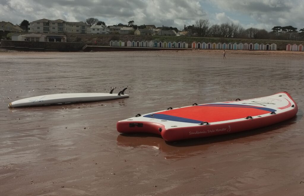 Velký červenobílý nafukovací paddleboard položený na mokré pláži.