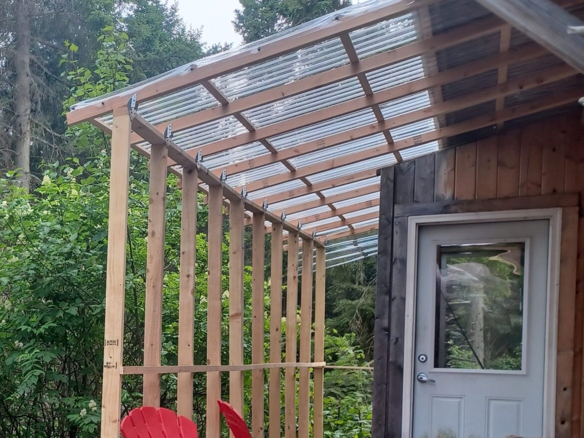 Dřevěná pergola s průhlednou polykarbonátovou střechou nad venkovním posezením.