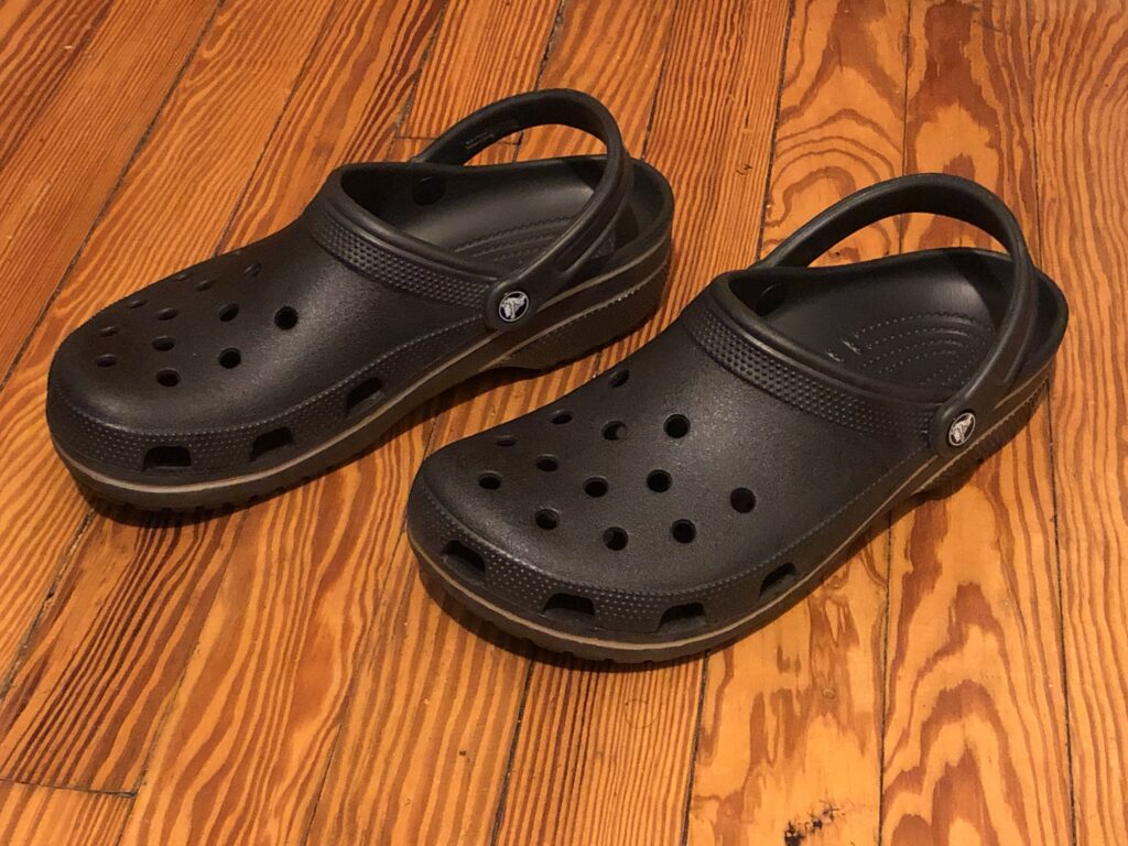 Černé pěnové pantofle typu Crocs na dřevěném povrchu.