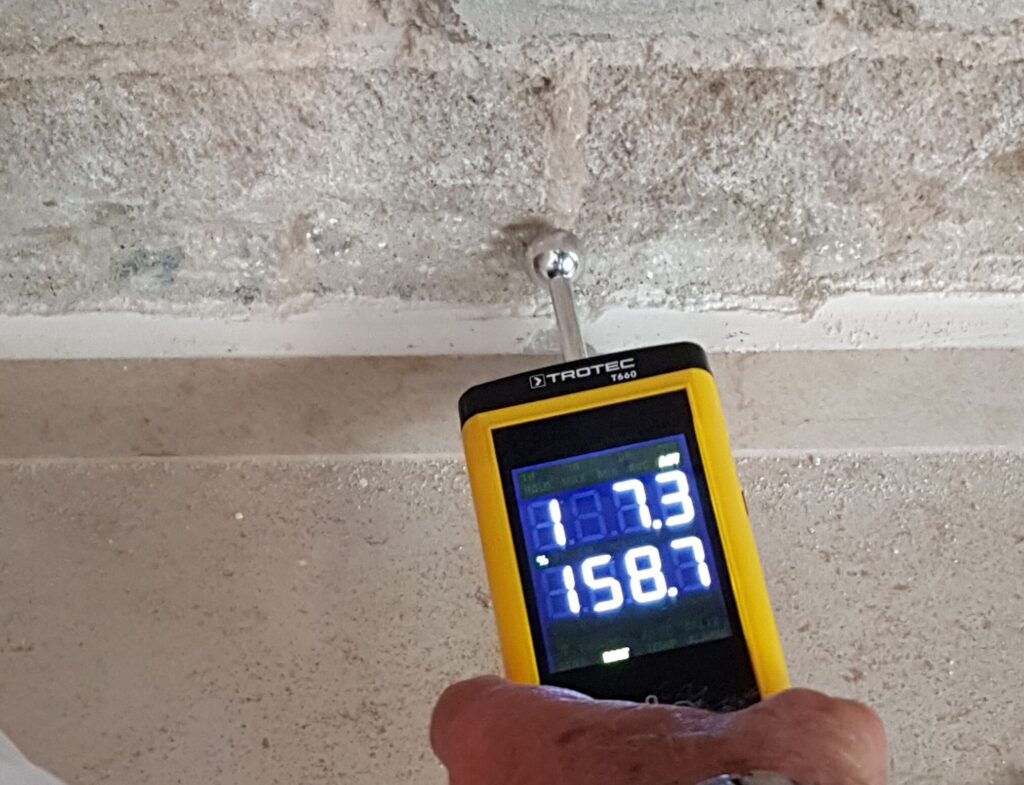 Ruka drží vlhkoměr při měření vlhkosti materiálu