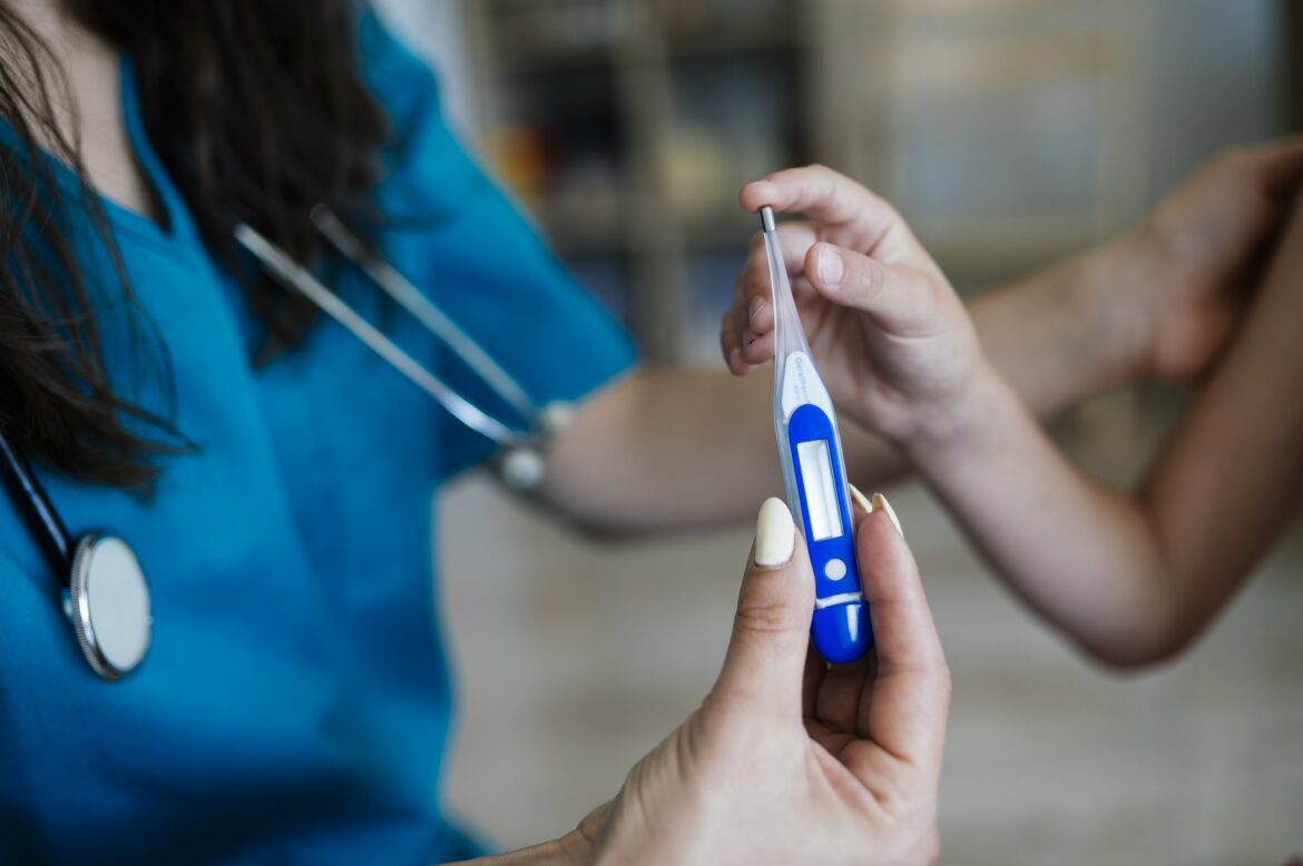 Zdravotnice měří teplotu digitálním teploměrem u dítěte s podezřením na chřipku