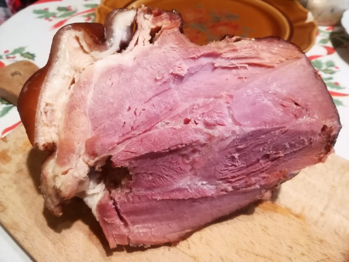 Řez růžovou šunkou s vrstvou bílého tuku na dřevěném prkénku
