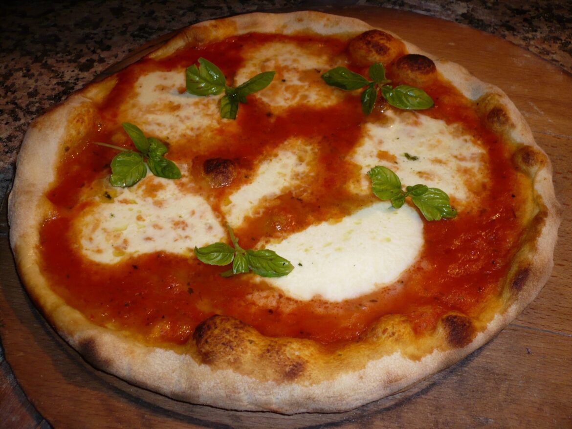 Upečená pizza s rajčatovou omáčkou, sýrem a lístky bazalky na dřevěném prkénku.