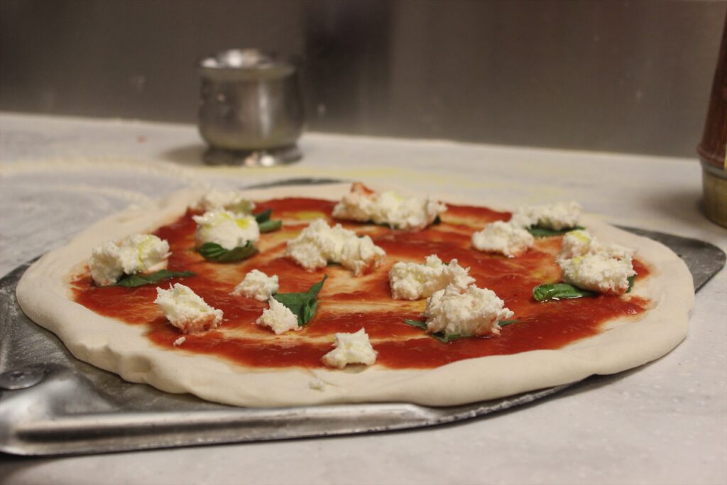 Neupečená pizza s rajčatovou omáčkou, bílým sýrem a bazalkou na kovové lopatě.