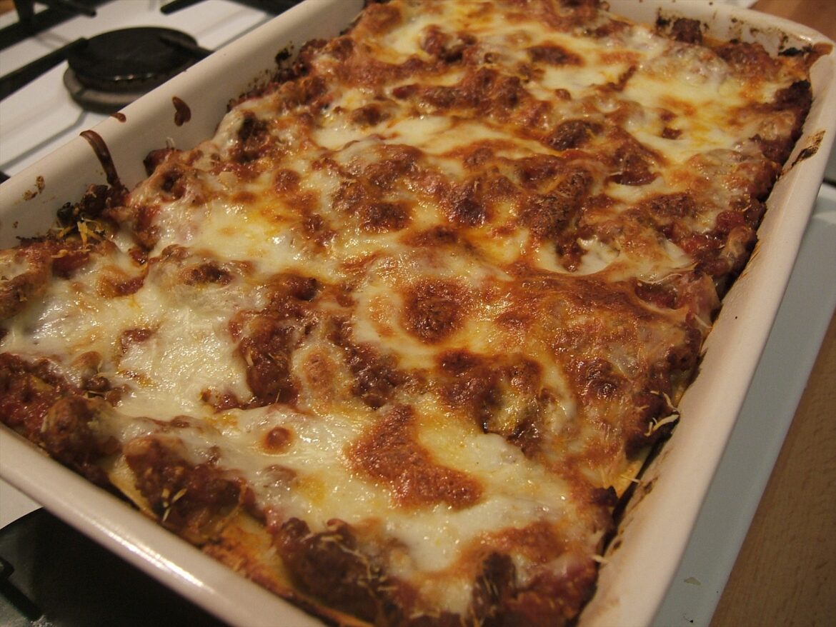 Zapečené lasagne v bílé obdélníkové nádobě položené na sporáku.