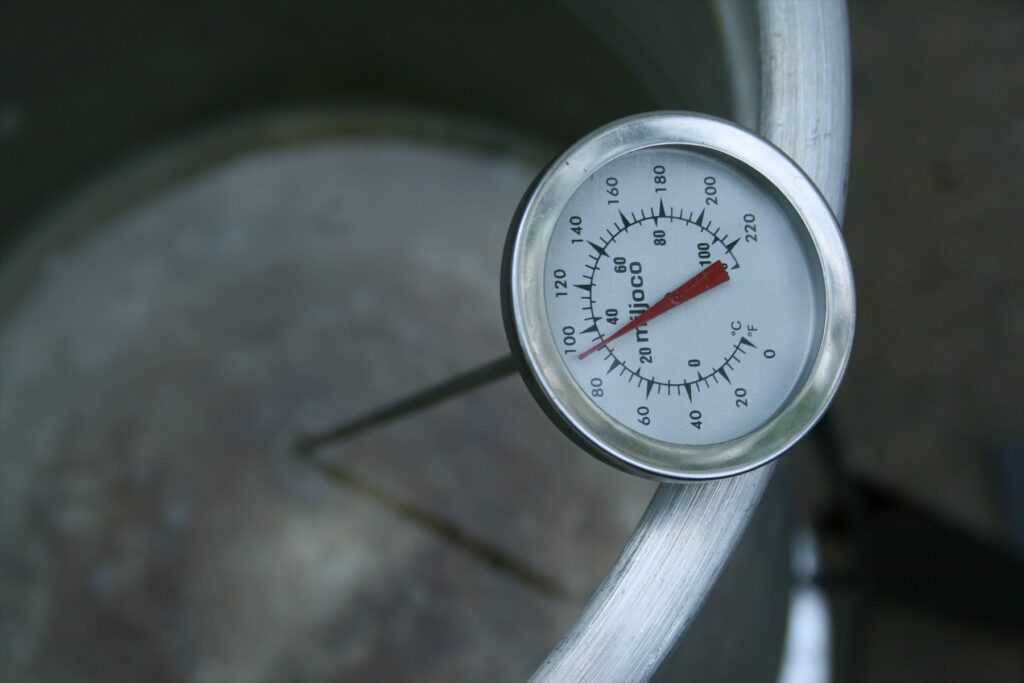 Ručičkový teploměr se stupnicemi °C a °F upevněný na okraji kovové nádoby.