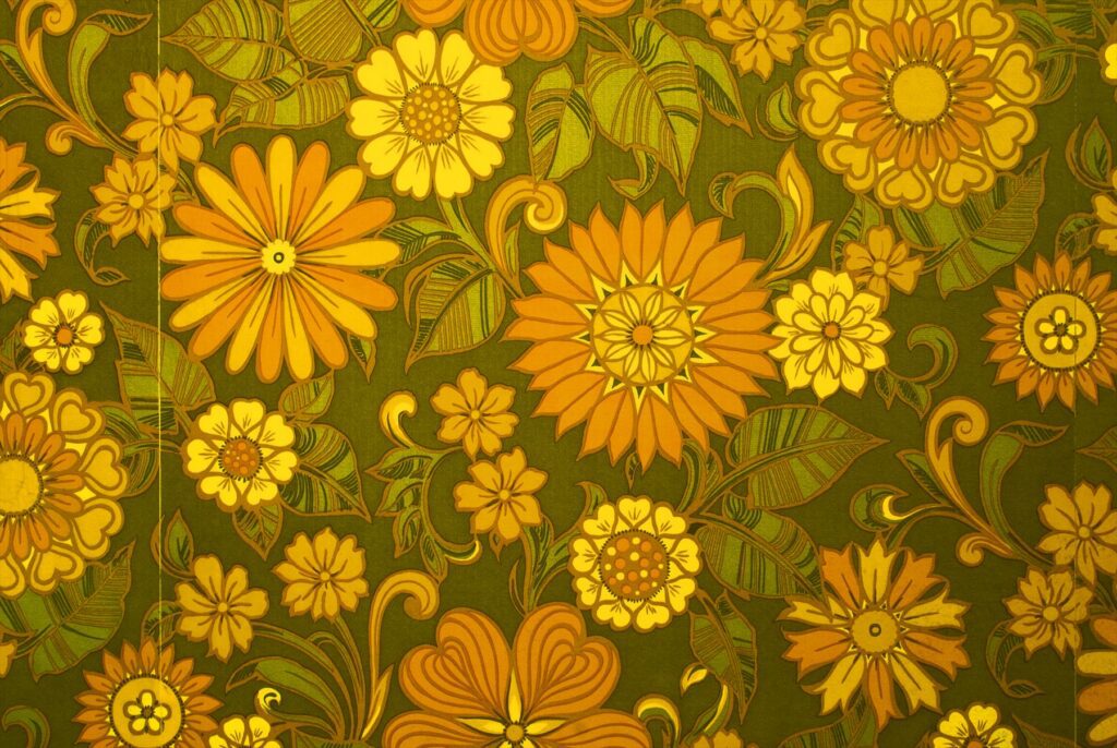 Detail tapety se žlutými a oranžovými květy a zelenými listy.