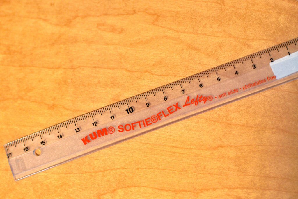 Průhledné pravítko pro leváky s centimetrovou a milimetrovou stupnicí na dřevěné ploše
