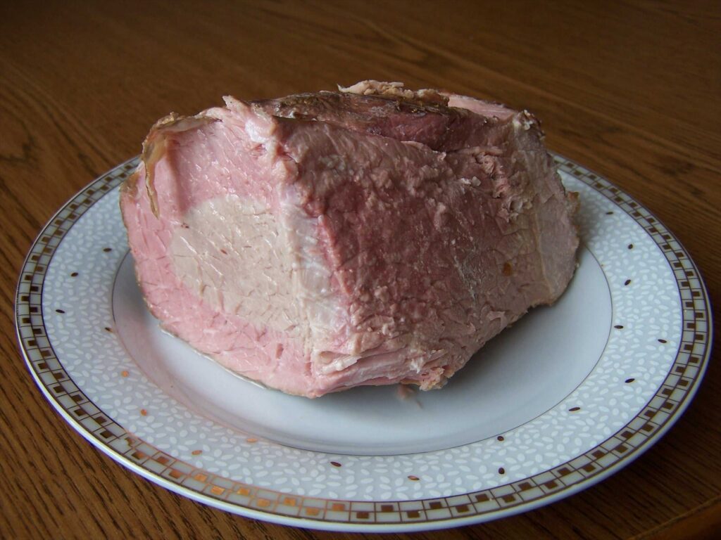 Kus růžové šunky na bílém talíři se zdobeným okrajem