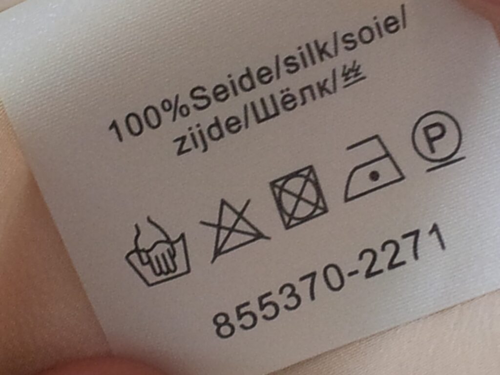 Štítek s údajem o hedvábí a symboly ručního praní, zákazu bělení a sušení v sušičce.