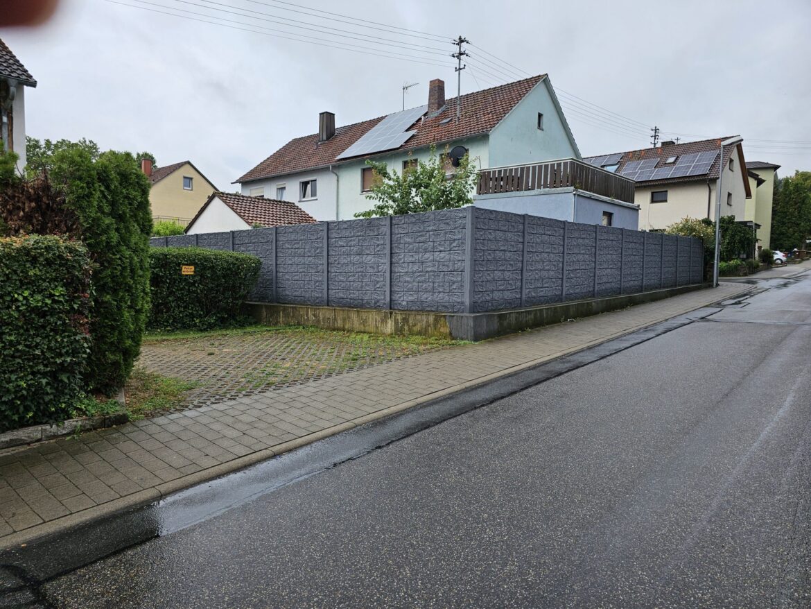 Vysoký betonový plot z prefabrikovaných desek s reliéfním vzorem kamene na hranici pozemku