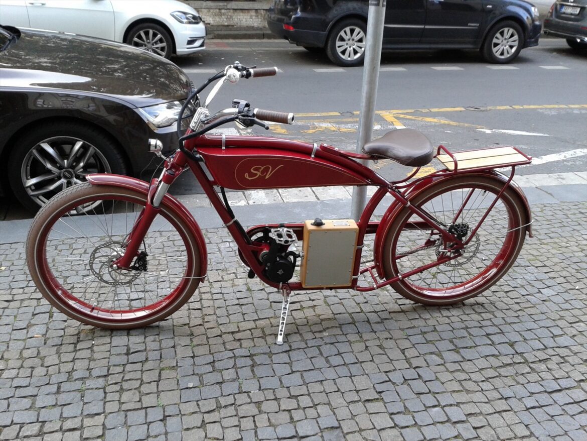 Červené městské elektrokolo SVBike s dřevěnou schránkou baterie stojící na chodníku.