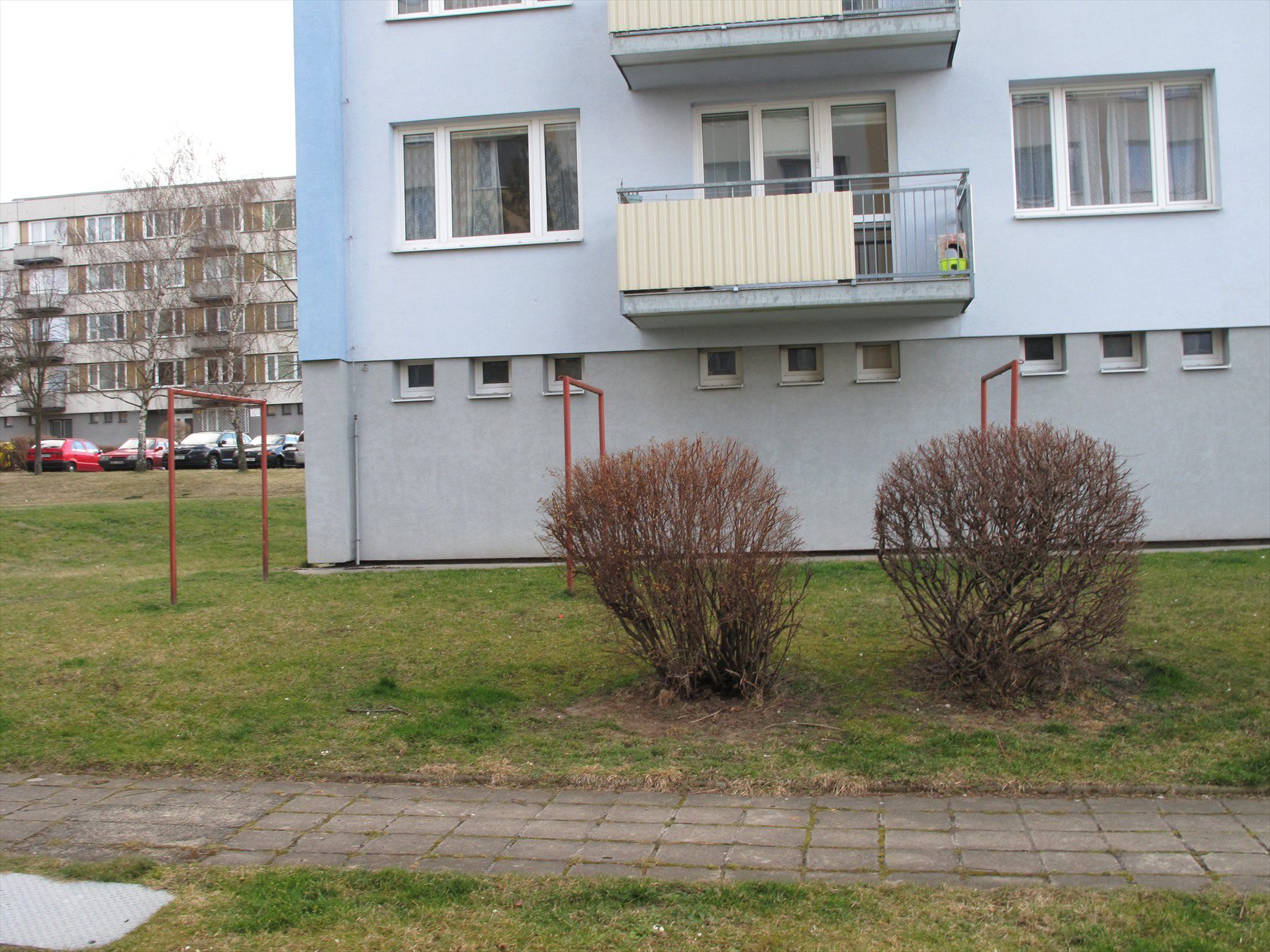 Spodní podlaží modrého panelového domu s balkony a keři v Písku