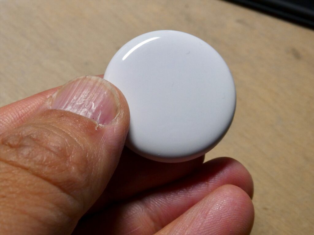 Bílá strana lokátoru Apple AirTag drženého mezi prsty.