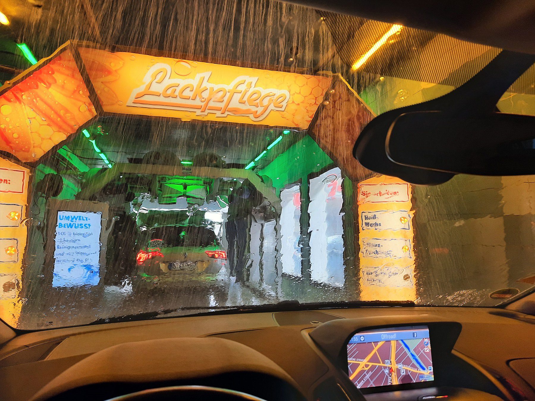 Pohled přes mokré čelní sklo na vůz a mycí zařízení v automatické myčce.