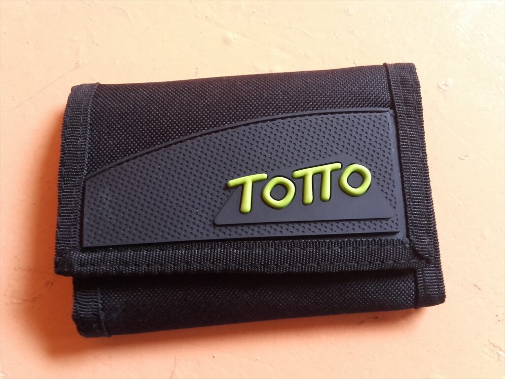 Zavřená černá textilní peněženka s nápisem Totto na světlém podkladu.