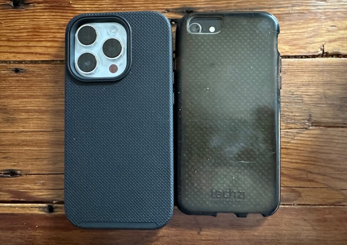Zadní strany iPhonu 14 Pro a iPhonu 8 v pouzdrech na dřevěném stole