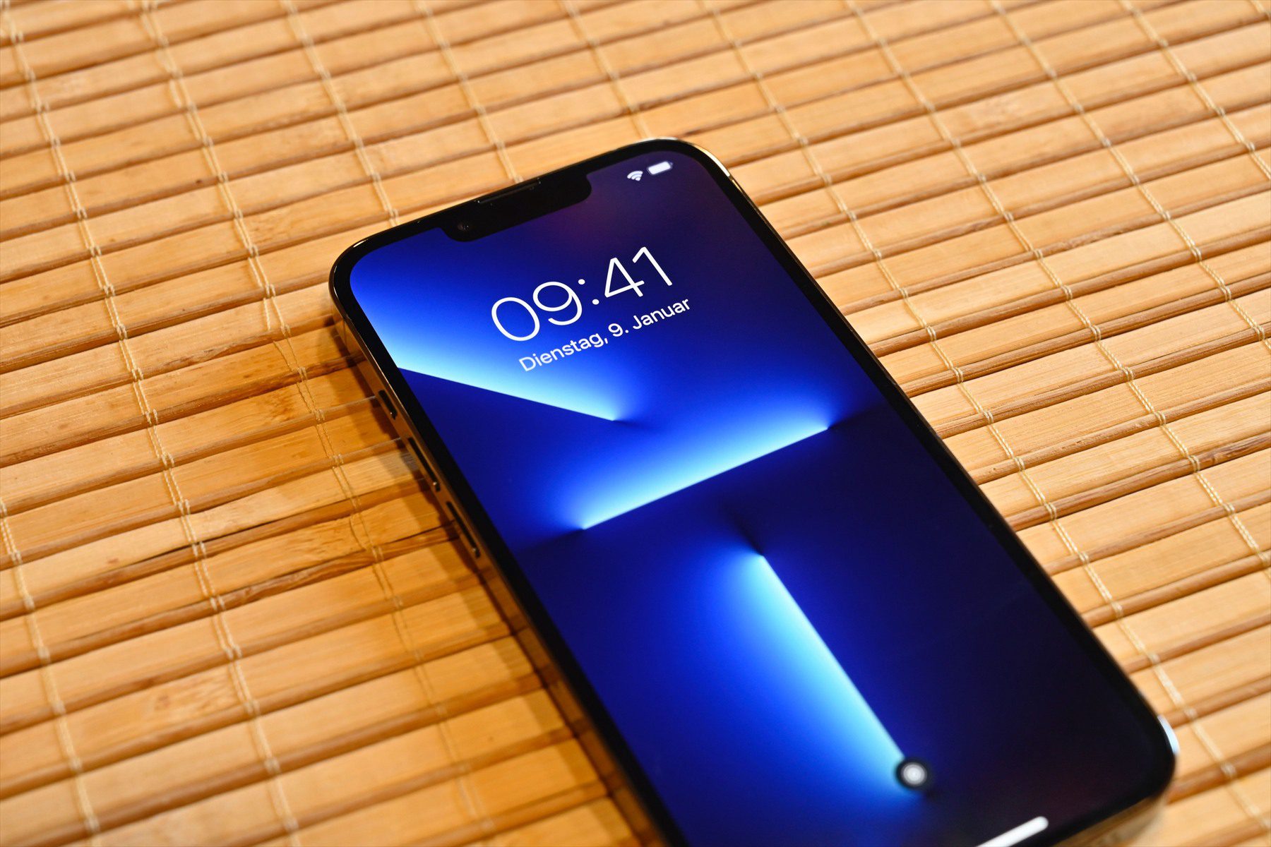 iPhone 13 Pro se zamknutou obrazovkou na bambusové podložce