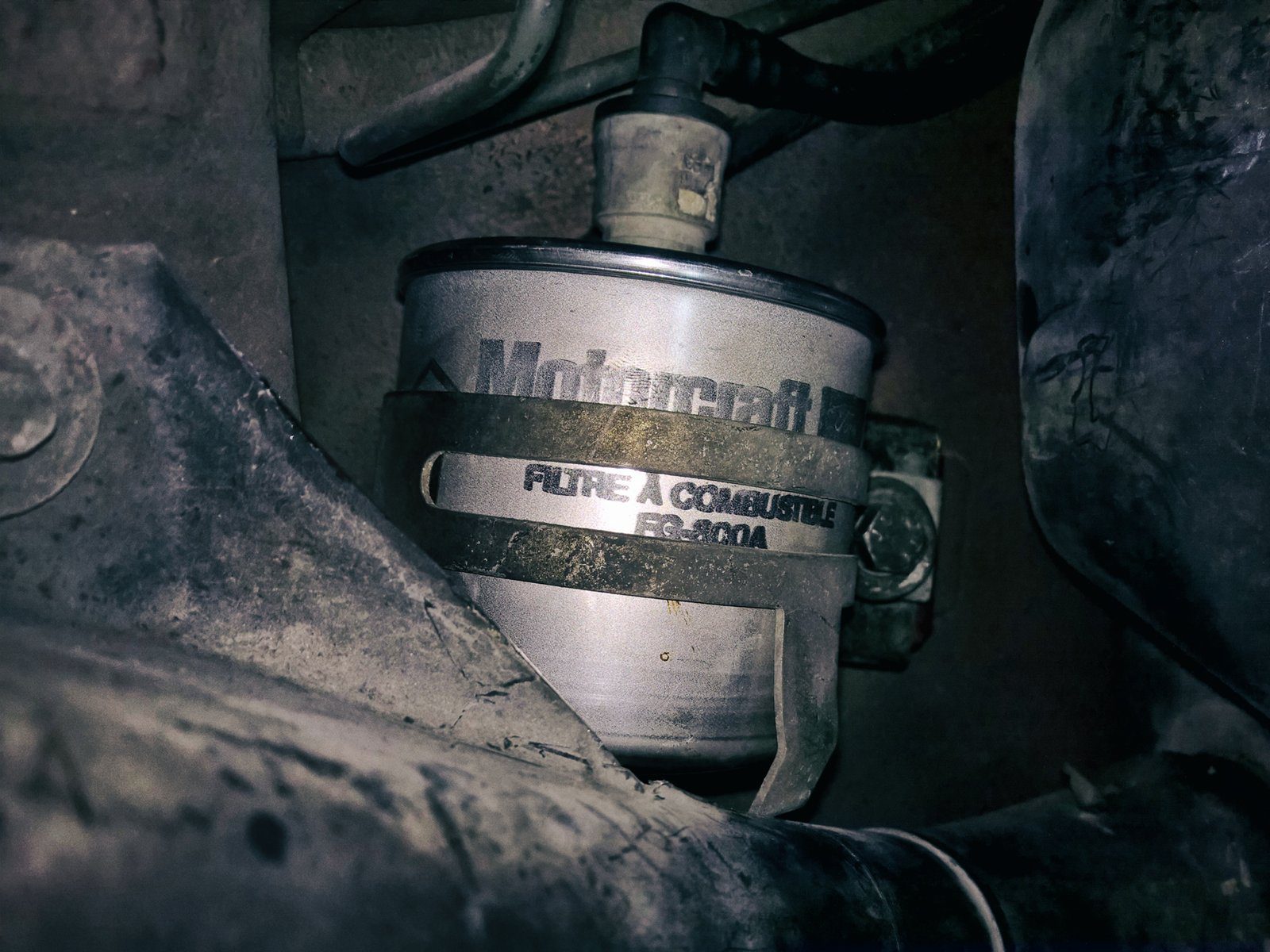 Detail kovového palivového filtru napojeného na palivové vedení automobilu.