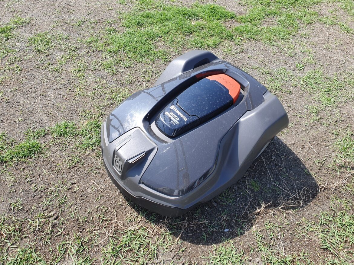 Moderní robotická sekačka na trávu stojící na zeleném posekaném trávníku v zahradě