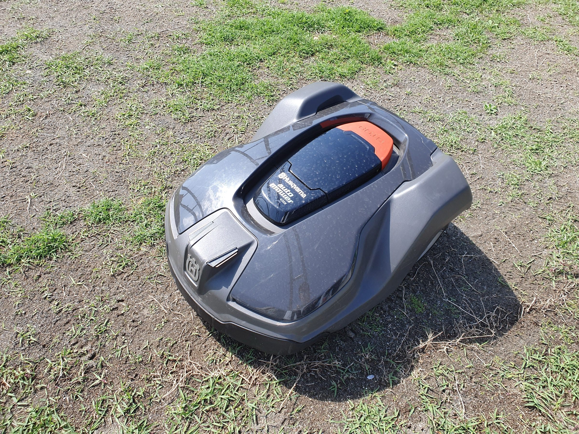 Moderní robotická sekačka na trávu stojící na zeleném posekaném trávníku v zahradě