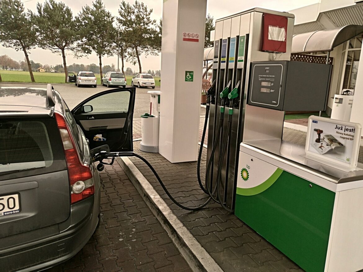 Osobní automobil u stojanu čerpací stanice se zasunutou tankovací pistolí v hrdle nádrže.