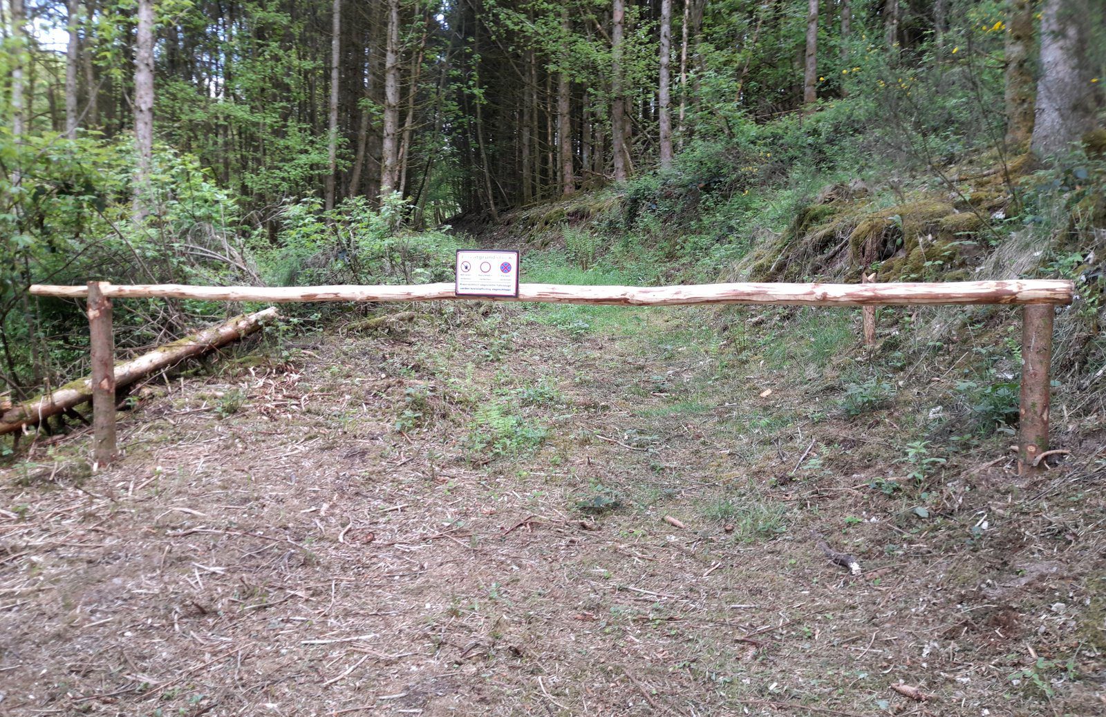 Spuštěná dřevěná závora přehrazující štěrkovou příjezdovou komunikaci.